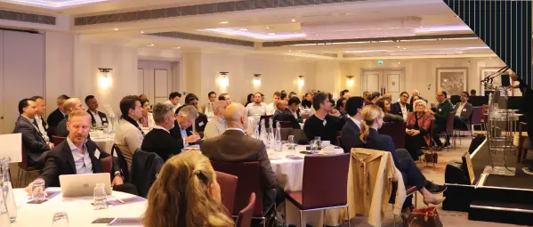 A conference or seminar setting with attendees seated at round tables, participating in a session.
